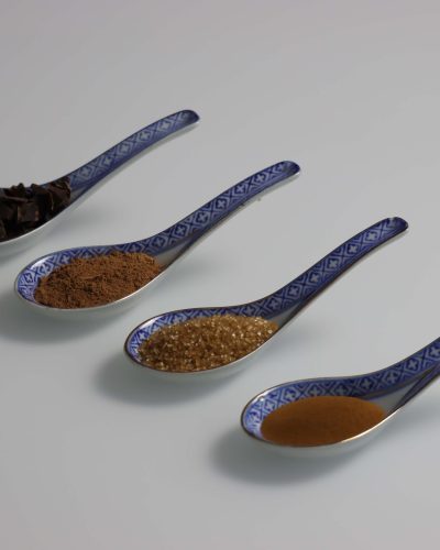 Četiri porculanske žličice s čokoladom, kakaom, smeđim šećerom i začinom, fotografija sastojaka na svijetloj podlozi