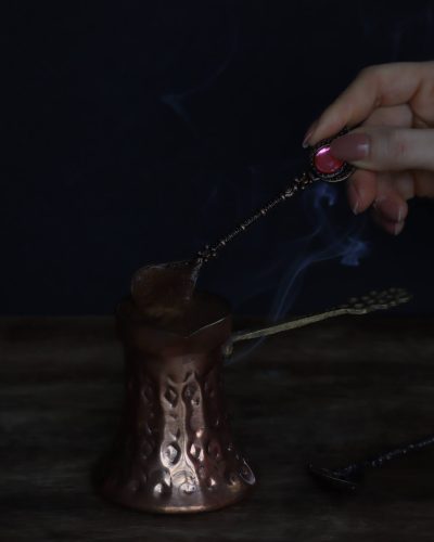 Ruka koja miješa kavu u bakrenoj džezvi, fotografija pripreme kave u tamnom