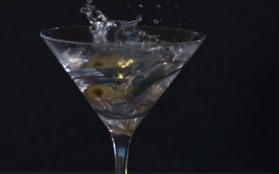 Martini čaša s maslinom i efektom prskanja, fotografija koktela u pokretu u tamnom ambijentu
