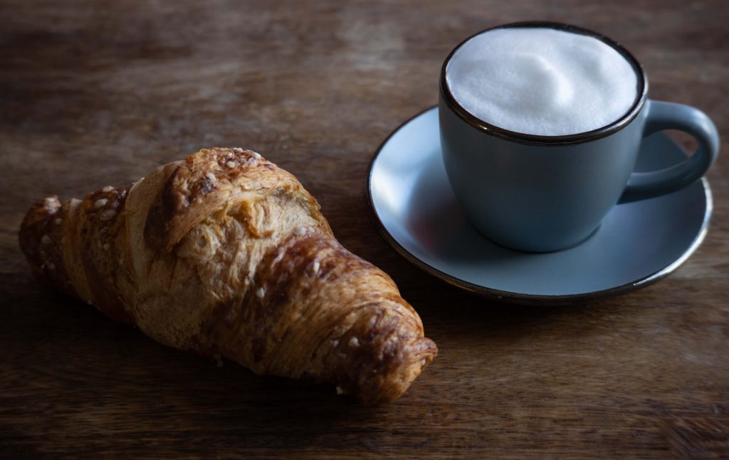 Kroasan i šalica cappuccina, fotografija doručka u prirodnom svjetlu