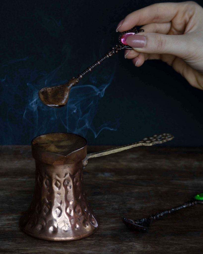 Ruka koja miješa kavu u bakrenoj džezvi, dim u fotografiji hrane